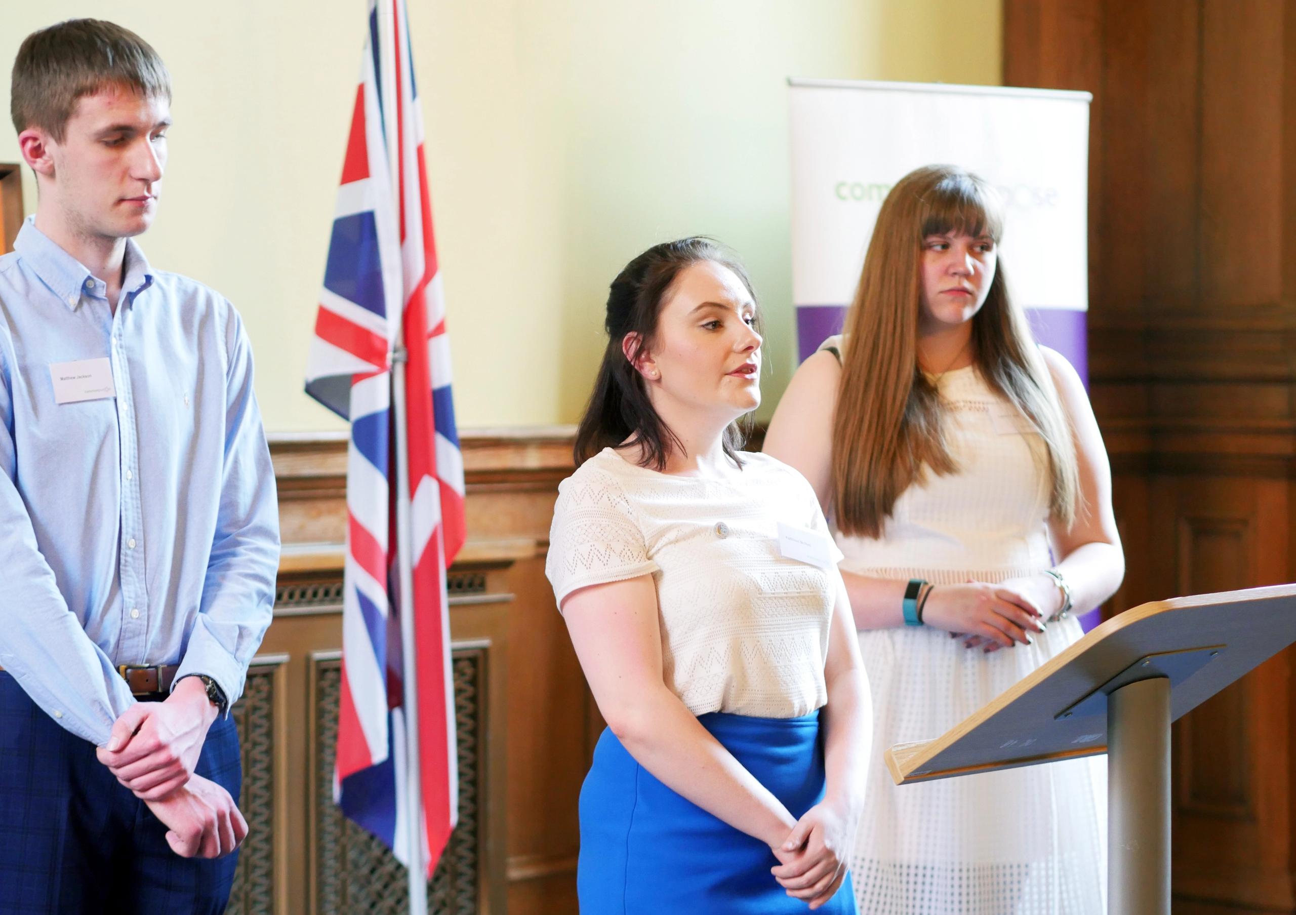 Three young people standing in front of a podium beside a British flag
